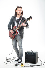 Concntrated young male guitarist playing electric guitar and using amplifier