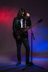 Obraz premium Singer with long hair singing in microphone and playing guitar