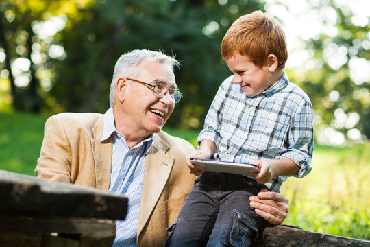 Grandfather and grandson are using digital tablet in park