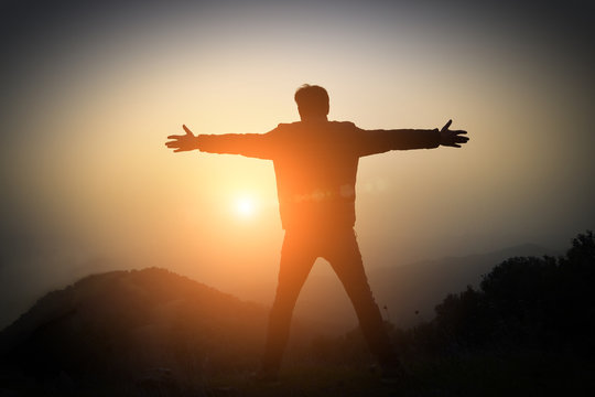 man with arms raised at sunset in the mountains