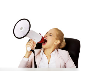 Business woman sitting behind the desk and screaming through a megaphone