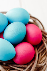 Fototapeta na wymiar blue and pink Easter eggs in nest on white wooden background