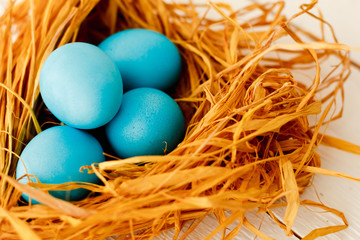 blue Easter eggs in nest on white wooden background