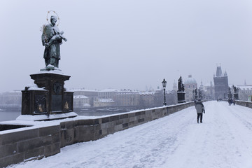 Fototapeta na wymiar Snowy foggy Prague Charles Bridge with its baroque Sculptures with Old Town, Czech Republic