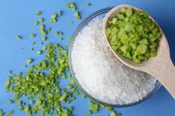 fragrant white sea salt is in a glass bowl . Scattered around the green salt on a blue wooden table