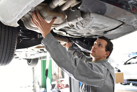 Mechaniker in einer Autowerkstatt kontrolliert Abgasanlage / Endschalldämpfer / Dieselpartikelfilter eines Fahrzeuges