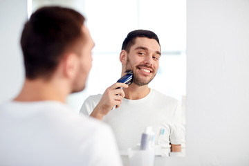 man shaving beard with trimmer at bathroom