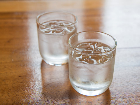 Glass water with ice on wooden table.