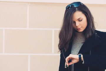 Beautiful young woman in a black coat checks the time on the clo