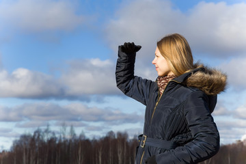 Happy, young girl looking somewhere in sunny spring and breathing fresh air on sky clouds background