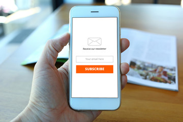 Hand holding smartphone with receive newsletter form on cafe bac