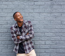 Black man smiling with arms crossed against gray wall