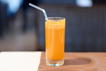 A glass with fresh carrot and apple juice with straw