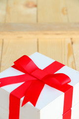 Gift box with red bow on wooden background.