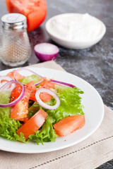 Salad with greens, tomatoes, red onions and cucumber on white pl