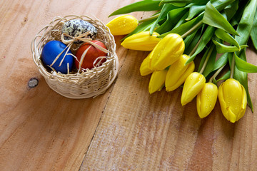 Easter basket with colored eggs and yellow tulips.