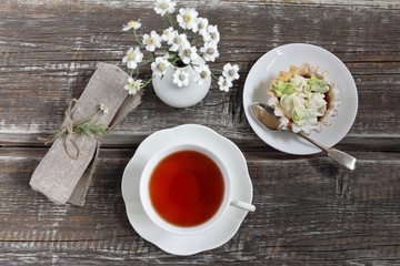 cup of tea, a cake, a bouquet of  camomiles, a napkin on a wooden background