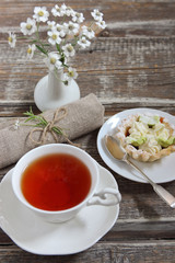 cup of tea, a cake, a bouquet of  camomiles, a napkin on a wooden background