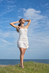 Girl in white dress posing with arms raised on background of sky