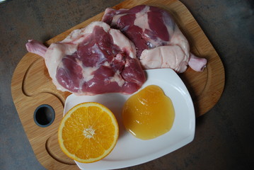 Fresh duck legs with orange and honey on a wooden board.