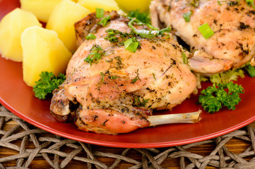 Oven baked rabbit with potatoes on red plate on wooden table.