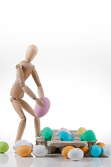 Burattino di legno che posa uova di Pasqua colorate in un contenitore di cartone