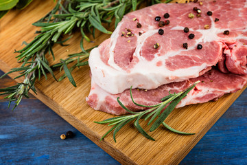 Close up wooden chopping board with raw meat  with herbs andspices on a blue  rustic table
