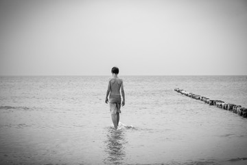 bw shot of a teenage boy who is walking into the sea