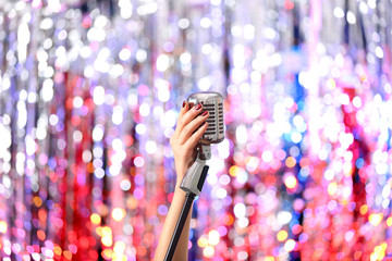 Female hands holding microphone against bright glitter background