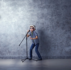 Little boy singing with microphone on a grey wall background