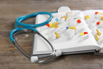 Stethoscope with pills and book on wooden table