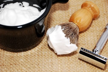 Shaving brush with foam, razor and mug on a burlap background