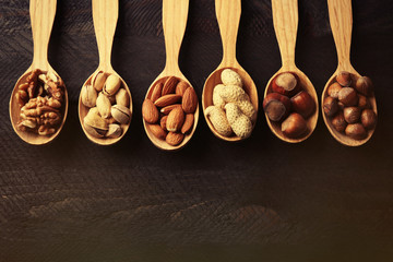 Spoons with hazelnuts, walnuts, pistachios, almonds, acorns and peanuts, on grey wooden background