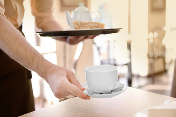 Waiter serving tea to customer in cafe