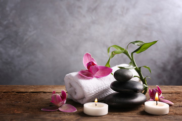 Spa stones with candles, purple orchid, bamboo and towel on wooden table against grey background