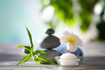 Fototapeta na wymiar Spa stones with towel, tropical flower, bamboo and candle on blurred background