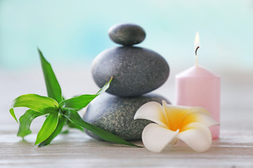 Fototapeta na wymiar Spa stones with candle, bamboo and tropical flower on blurred background
