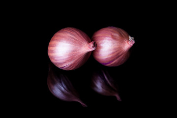 Two shallot onions with shell on black background with reflection