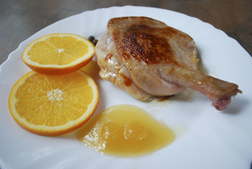 Cooked duck leg with orange and honey on white dish.