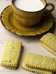 Biscotti e tazza di latte per colazione semplice su tavolo di legno