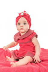 Portrait of a baby girl nice dressed in red clothes looking for attention while sitting on her bed