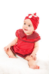 Portrait of young 1 year old baby girl in red dress with red hat on her head looking away, shot against white background