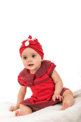 Young child dressed in red clothes sitting on blanket against white background