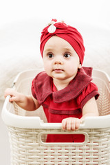 Vertical portrait of 1 year old little girl on white background inside laundry basket looking up