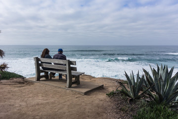 Young Couple Sit on Bench Looking Out Over Ocean