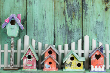 Row of colorful birdhouses by white picket fence