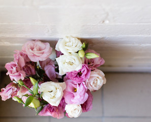 High angle view of pink and white lisianthus flowers against a white brick wall with dirty tile floor
