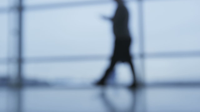 One person walking in office hallway using smartphone. Business woman out of focus blurred defocused background shot in slow motion.