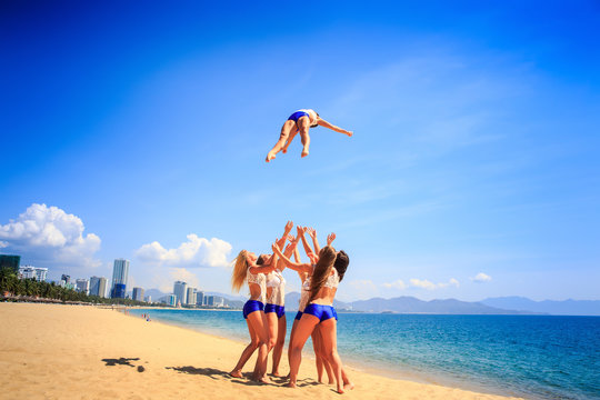 cheerleaders in uniform perform Toe Touch Basket Toss on beach