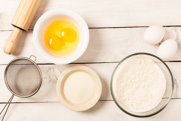 Baking in rustic kitchen recipe ingredients (eggs, flour, milk) on white  wooden table from above. 
